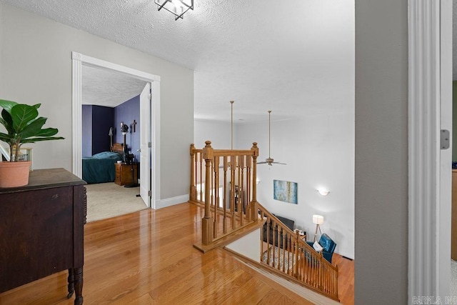 corridor with baseboards, a textured ceiling, an upstairs landing, and wood finished floors