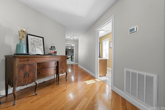 corridor featuring visible vents, light wood-style flooring, and baseboards