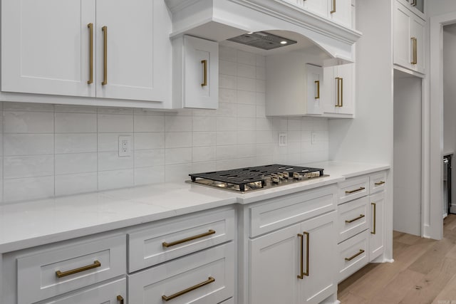 kitchen with tasteful backsplash, white cabinets, light wood-style flooring, and light stone countertops