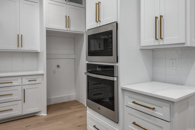kitchen featuring light stone counters, built in microwave, white cabinets, and oven