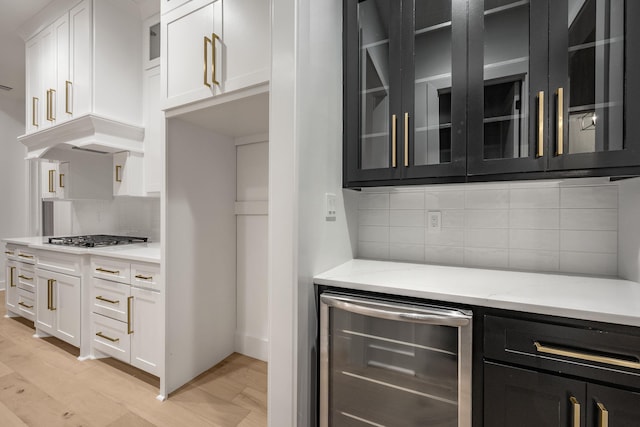 kitchen with stainless steel gas cooktop, wine cooler, glass insert cabinets, and white cabinets