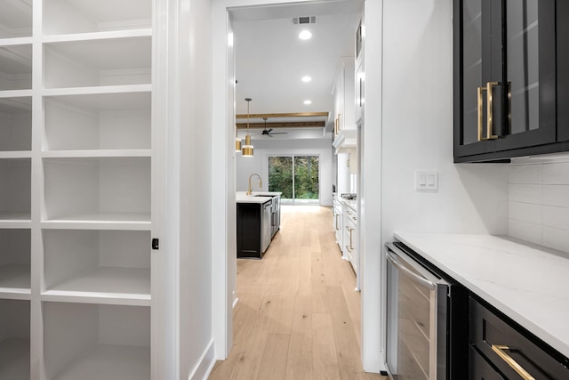 hall with light wood-style flooring, recessed lighting, beverage cooler, a sink, and visible vents