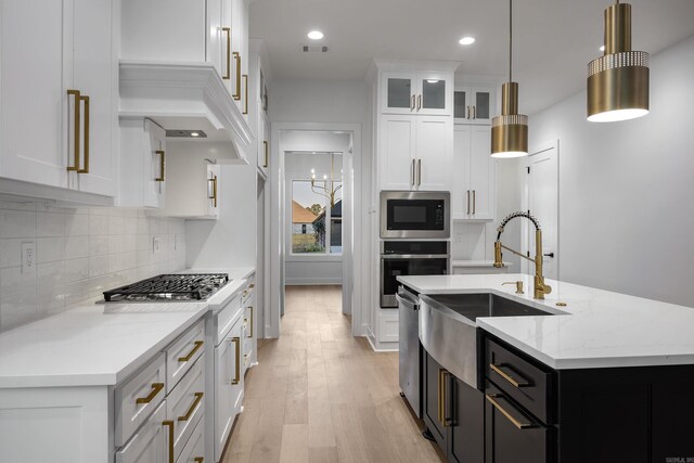 kitchen with dark cabinets, white cabinets, appliances with stainless steel finishes, an island with sink, and decorative light fixtures