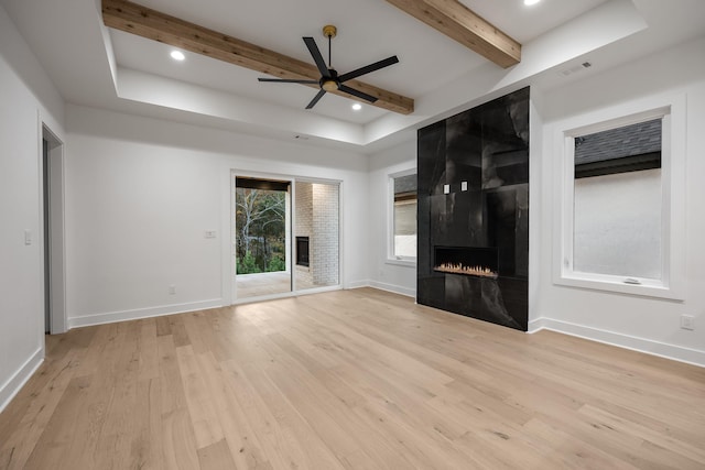 unfurnished living room featuring a large fireplace, light wood-style flooring, baseboards, and beamed ceiling