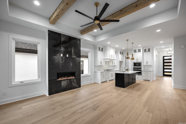 kitchen featuring glass insert cabinets, decorative light fixtures, a kitchen island with sink, light countertops, and white cabinetry