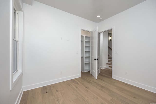 unfurnished bedroom with a walk in closet, light wood finished floors, recessed lighting, a closet, and baseboards
