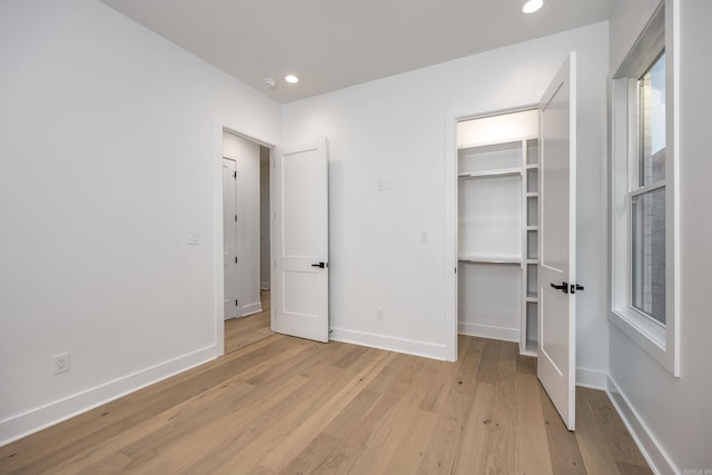 unfurnished bedroom with recessed lighting, a walk in closet, light wood-style flooring, and baseboards