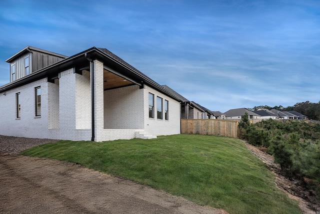 view of side of property featuring board and batten siding, fence, a lawn, and brick siding