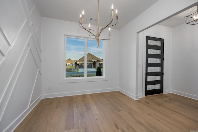 unfurnished dining area with an inviting chandelier, visible vents, baseboards, and wood finished floors