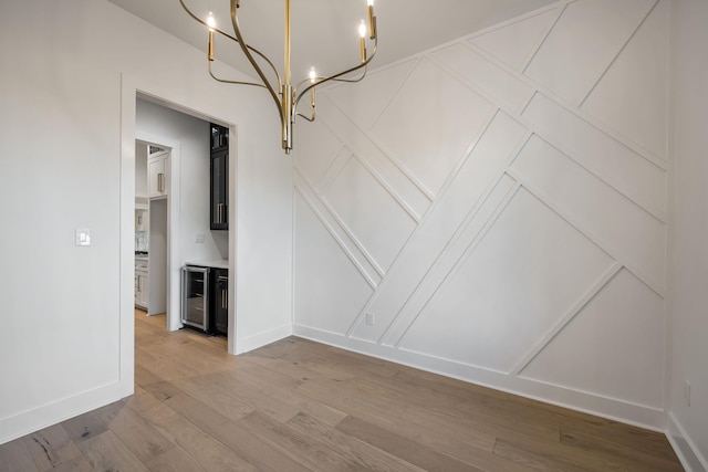 unfurnished dining area featuring beverage cooler, light wood finished floors, a chandelier, and baseboards