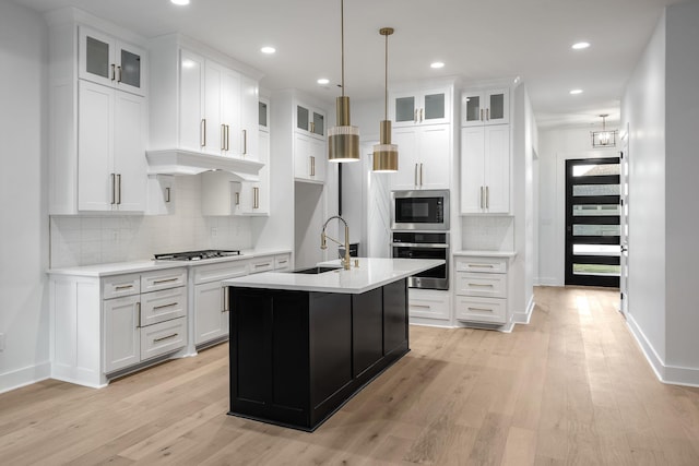 kitchen featuring an island with sink, white cabinetry, stainless steel appliances, and light countertops
