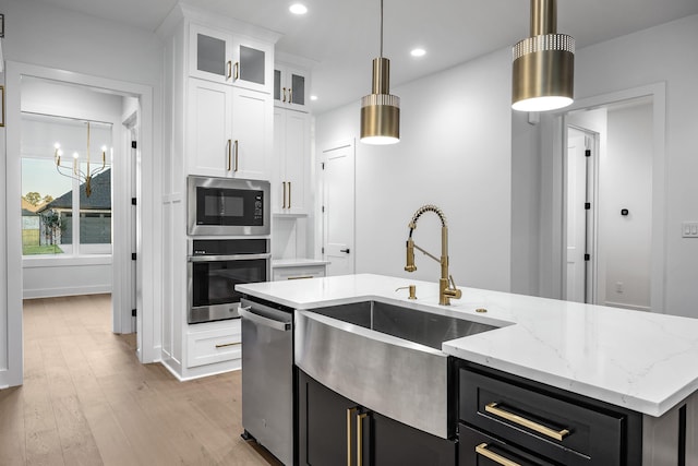 kitchen with a center island with sink, appliances with stainless steel finishes, dark cabinets, white cabinetry, and pendant lighting