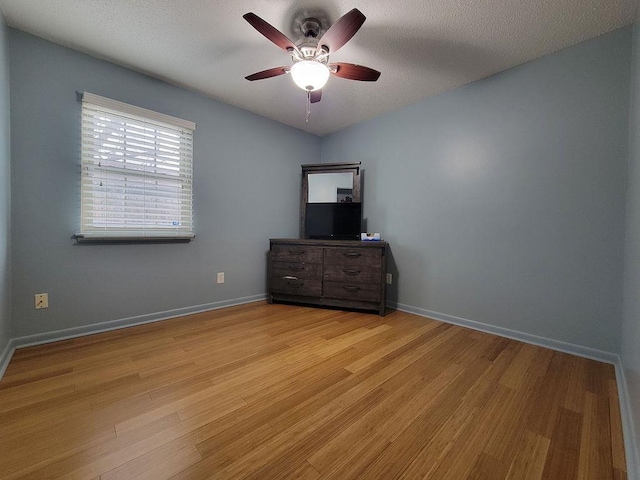 unfurnished room featuring light wood-type flooring, a ceiling fan, baseboards, and a textured ceiling