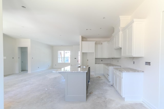 kitchen featuring baseboards, a kitchen island with sink, white cabinetry, and light stone counters