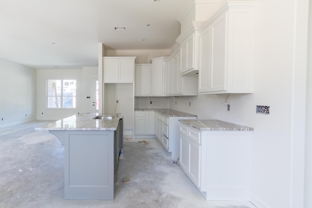 kitchen with light stone countertops, a center island with sink, white cabinets, and unfinished concrete floors