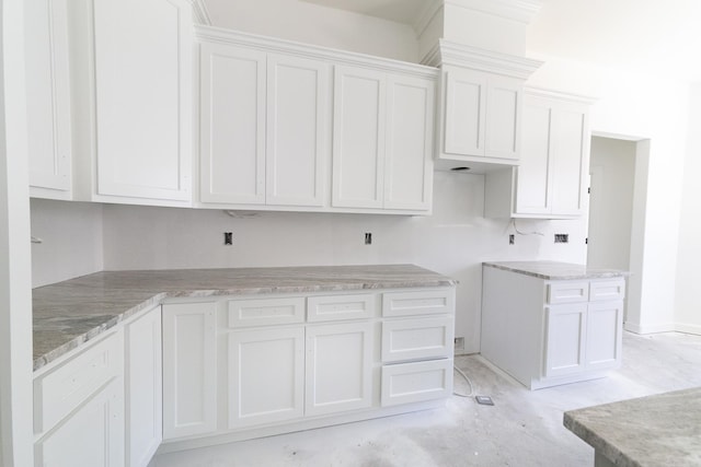 kitchen with concrete flooring, white cabinets, and light stone counters