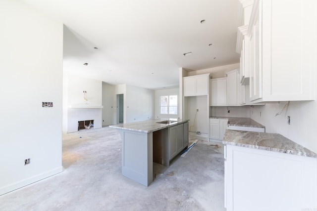 kitchen with open floor plan, light stone counters, a kitchen island, and white cabinets