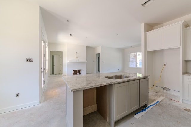 kitchen with open floor plan, light stone counters, a center island with sink, and white cabinets