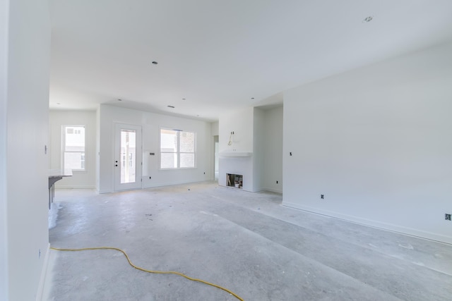 unfurnished living room featuring unfinished concrete flooring, a fireplace, and baseboards