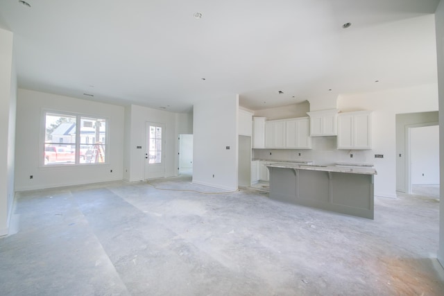 kitchen featuring unfinished concrete flooring, a spacious island, light countertops, open floor plan, and white cabinetry