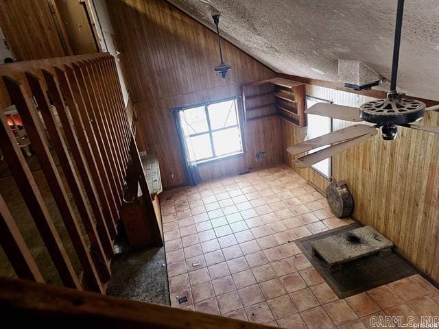 bonus room featuring light tile patterned floors, wooden walls, high vaulted ceiling, and a textured ceiling