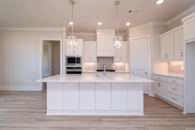 kitchen with pendant lighting, stainless steel appliances, light countertops, white cabinetry, and an island with sink