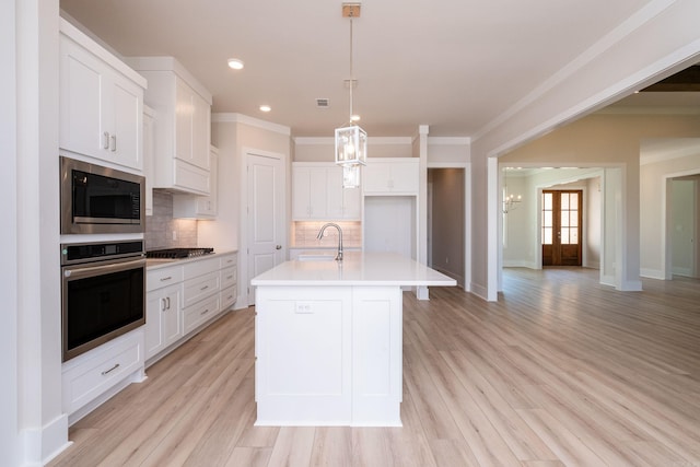 kitchen featuring a kitchen island with sink, a sink, white cabinetry, light countertops, and appliances with stainless steel finishes