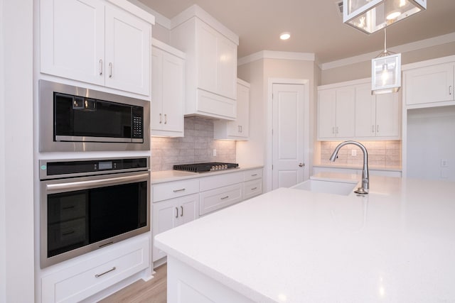 kitchen with a sink, stainless steel appliances, light countertops, and decorative light fixtures