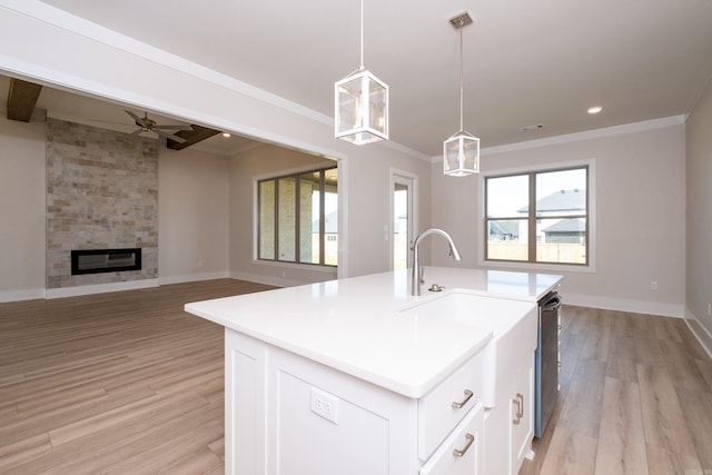 kitchen featuring pendant lighting, a center island with sink, open floor plan, white cabinets, and a large fireplace