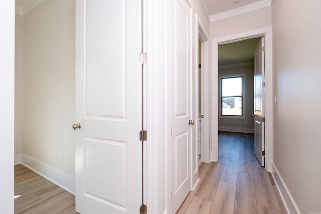 hall featuring light wood finished floors, baseboards, and ornamental molding