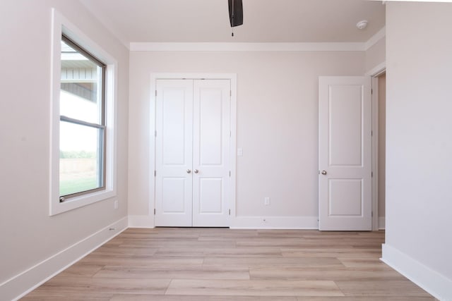 unfurnished bedroom featuring light wood finished floors, a closet, baseboards, and crown molding