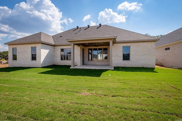 rear view of property with a shingled roof, a ceiling fan, a lawn, a patio area, and brick siding