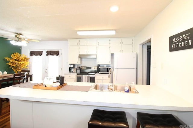 kitchen featuring stainless steel appliances, light countertops, white cabinetry, a peninsula, and under cabinet range hood