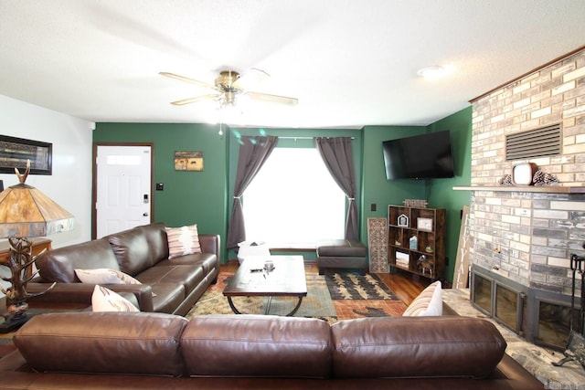 living room featuring ceiling fan, a fireplace, and wood finished floors