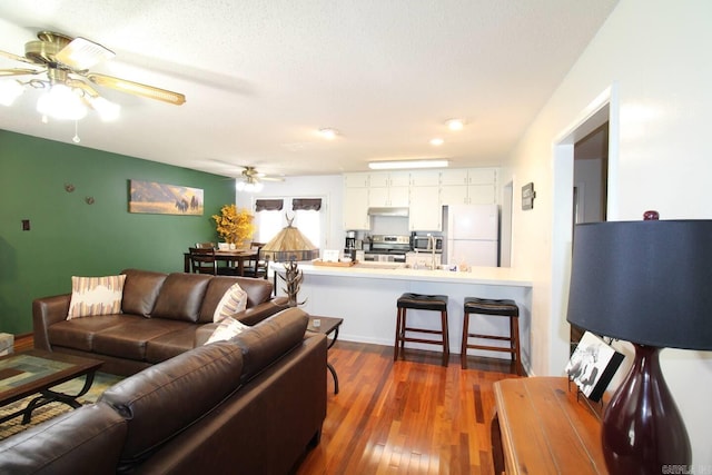 living room featuring ceiling fan, a textured ceiling, and dark wood-style floors