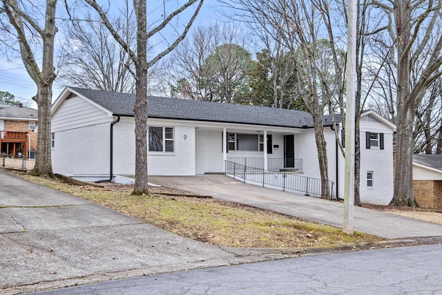 single story home with covered porch, driveway, brick siding, and roof with shingles