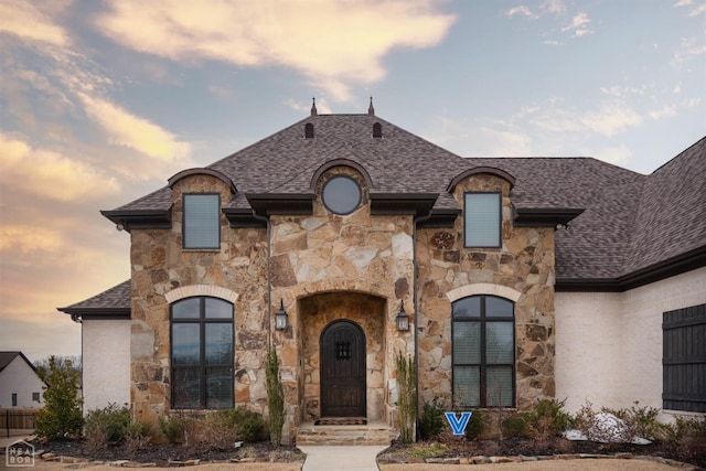 french country style house featuring stone siding and a shingled roof