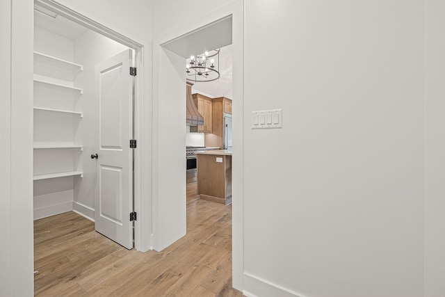 corridor with light wood finished floors, baseboards, and an inviting chandelier