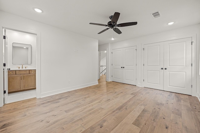 unfurnished bedroom featuring light wood finished floors, two closets, visible vents, ensuite bathroom, and a sink