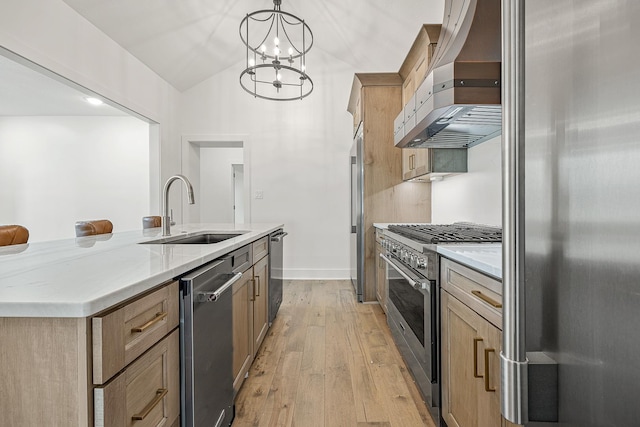 kitchen with premium appliances, hanging light fixtures, a kitchen island with sink, a sink, and wall chimney range hood