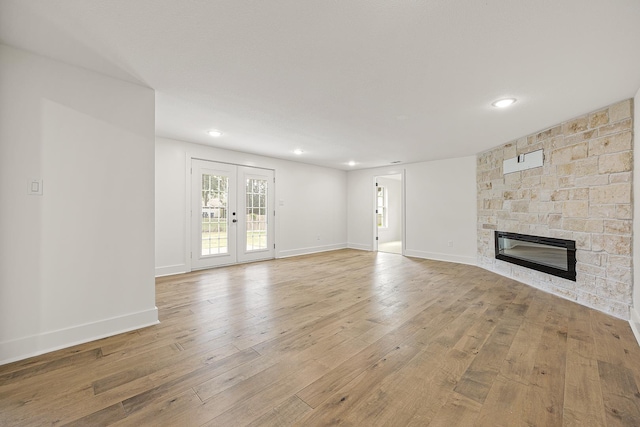 unfurnished living room featuring light wood-style floors, baseboards, french doors, and a stone fireplace