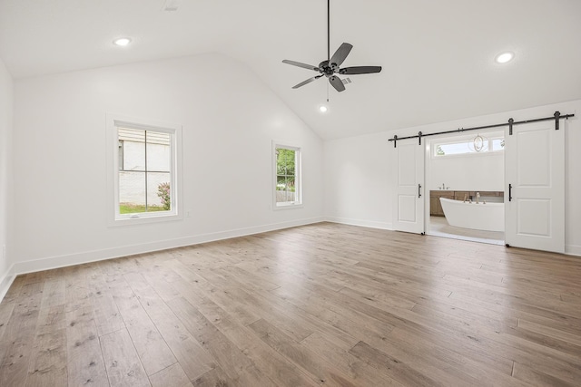 unfurnished living room with light wood finished floors, a barn door, baseboards, and a ceiling fan