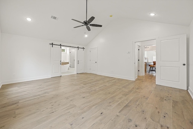 interior space with a barn door, visible vents, baseboards, a ceiling fan, and light wood finished floors