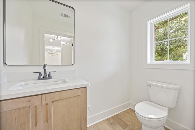 half bath with visible vents, toilet, vanity, wood finished floors, and baseboards