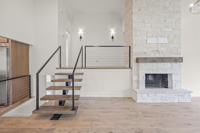 staircase with baseboards, a fireplace, a high ceiling, and wood finished floors