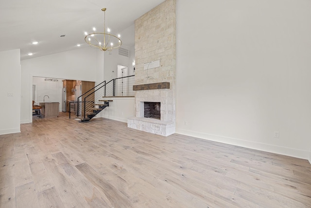 unfurnished living room with a fireplace, visible vents, light wood-style floors, high vaulted ceiling, and stairs