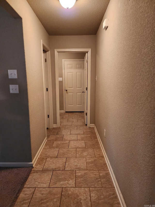 corridor featuring a textured ceiling, a textured wall, and baseboards