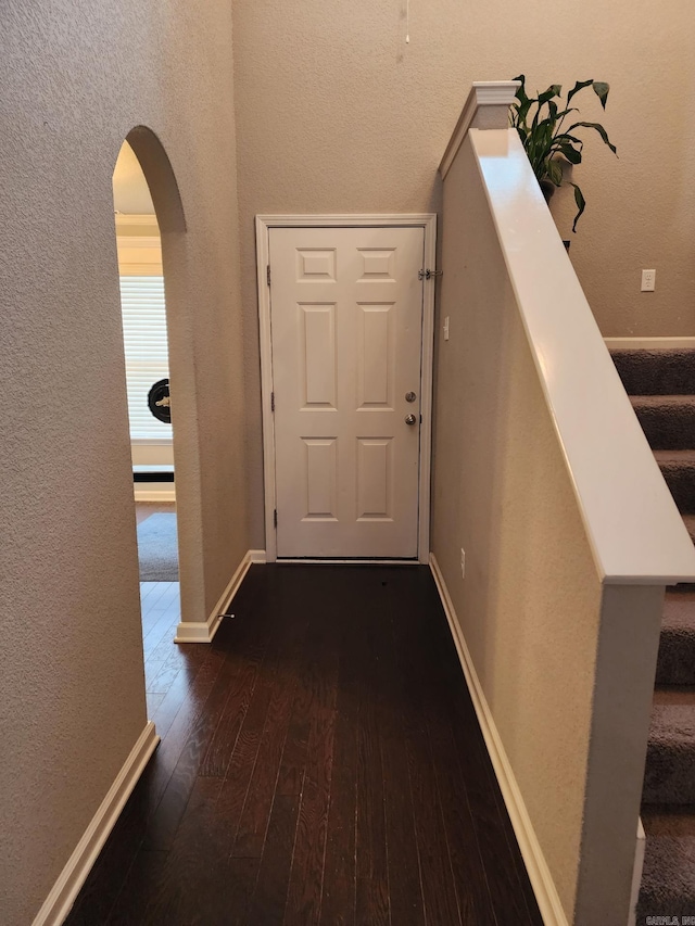 hallway with arched walkways, dark wood-type flooring, stairway, and baseboards