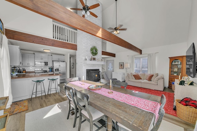 dining area featuring high vaulted ceiling, light wood-type flooring, beam ceiling, and a ceiling fan