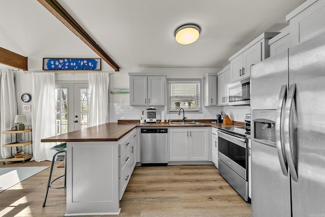 kitchen with light wood-style flooring, stainless steel appliances, a sink, white cabinetry, and a kitchen breakfast bar